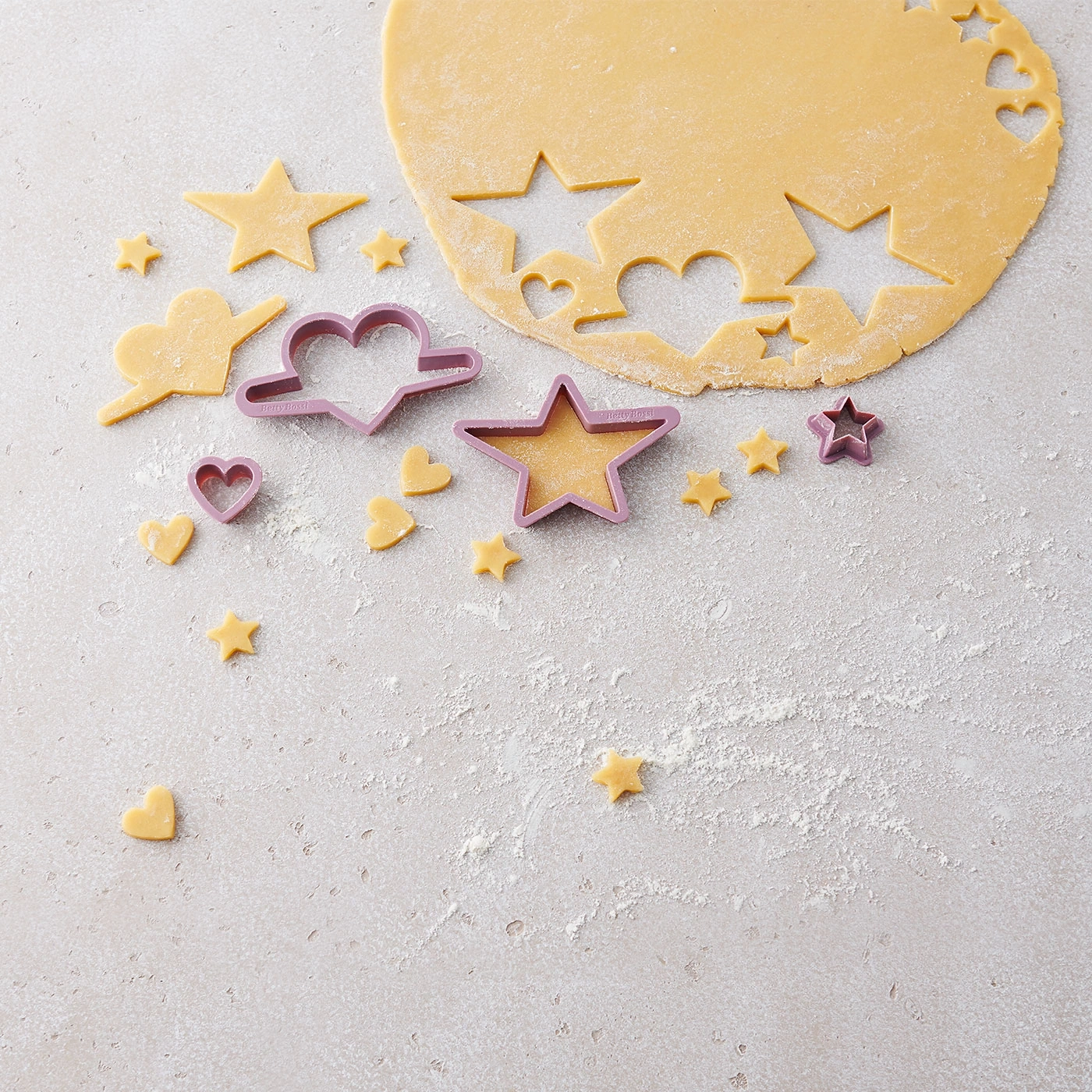 Découpage de biscuits avec des formes d'étoiles et de coeurs sur une surface farinée