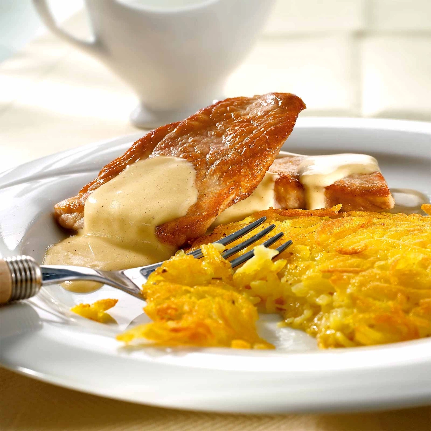 Gebratenes Fleisch mit Sauce und Rösti auf einem Teller mit Gabel.
