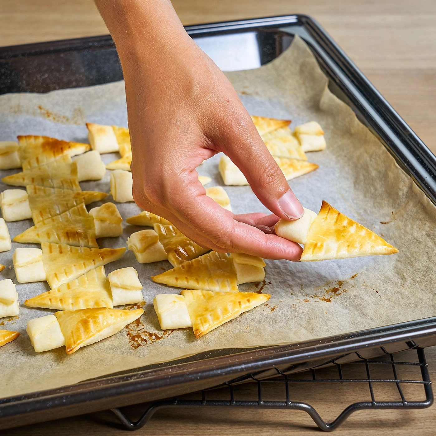 Hand nimmt Gebäck von Backblech, Gebäck in Form von Tannenbäumen