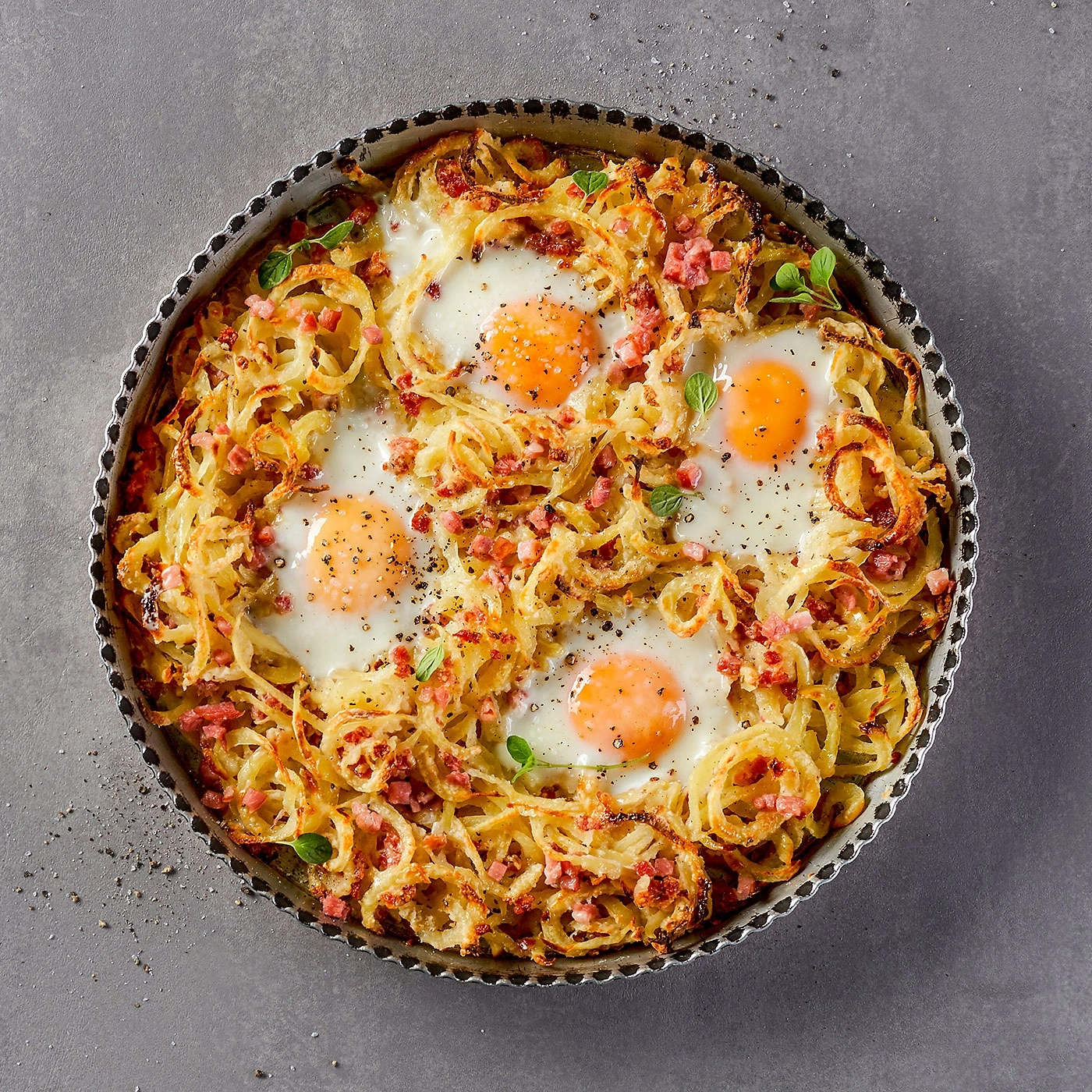 Gebratene Eier mit Kartoffeln und Speck in einer Kuchenform auf grauem Hintergrund.