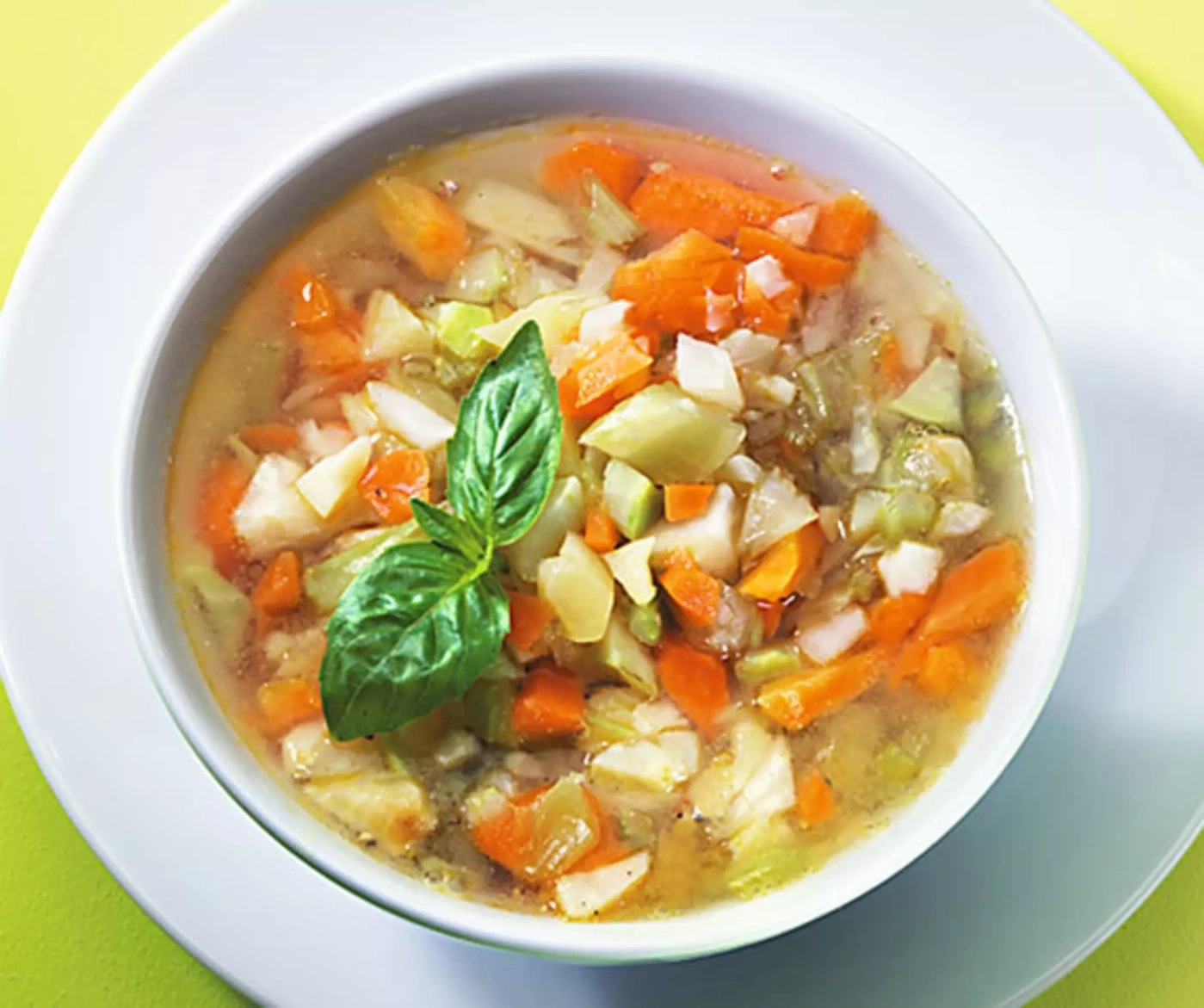 Un bol de soupe de légumes avec des carottes, du céleri et une garniture de feuilles de basilic.