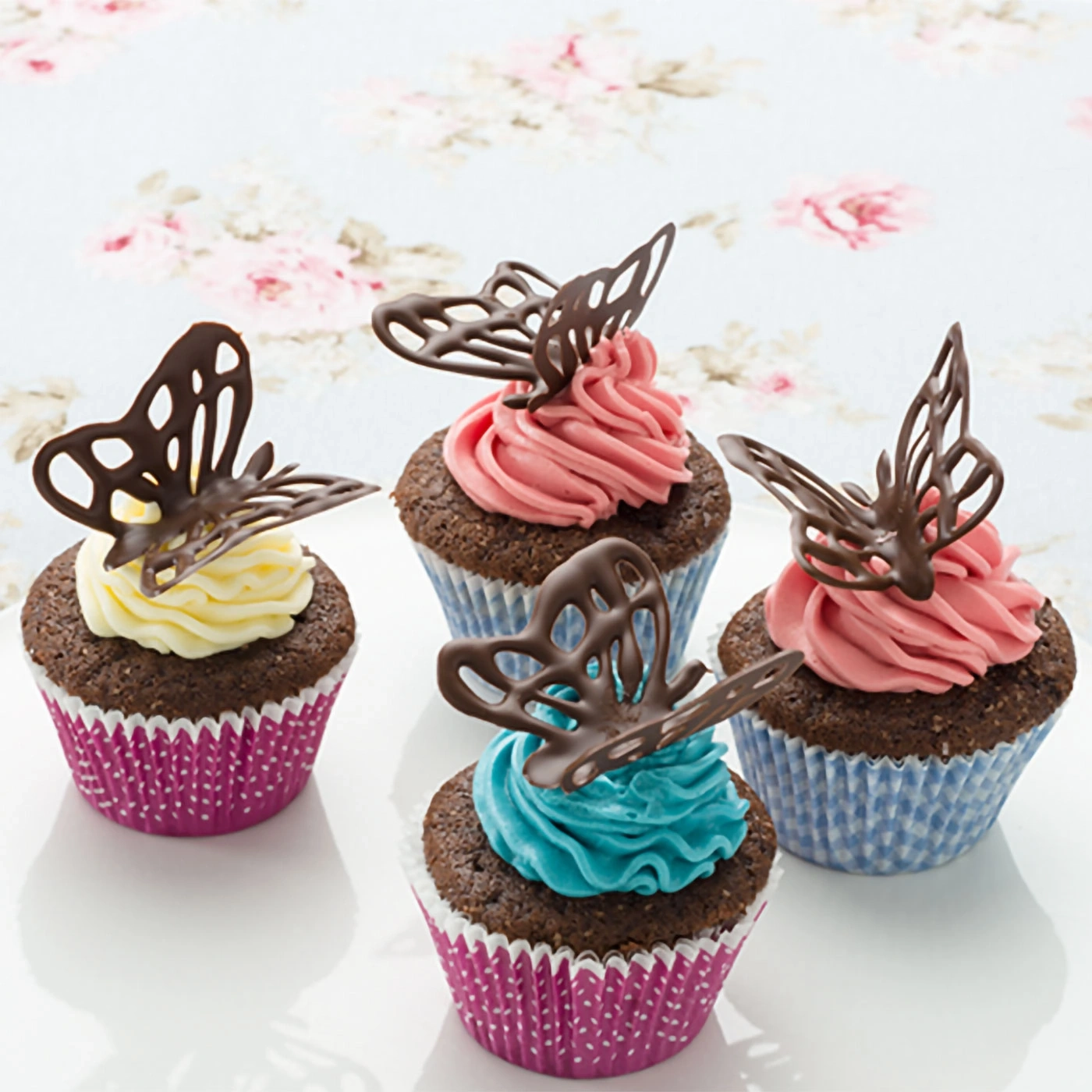 Cupcakes au chocolat avec décorations papillon et crème colorée sur une assiette.