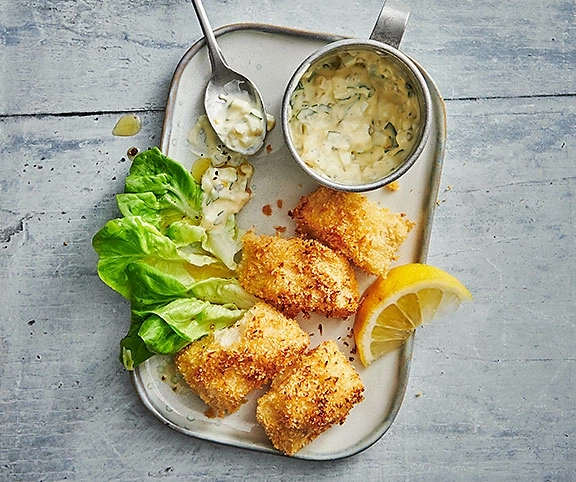 Gebratenes Fischgericht mit Salat, Zitrone und Sauce auf einem Tablett.