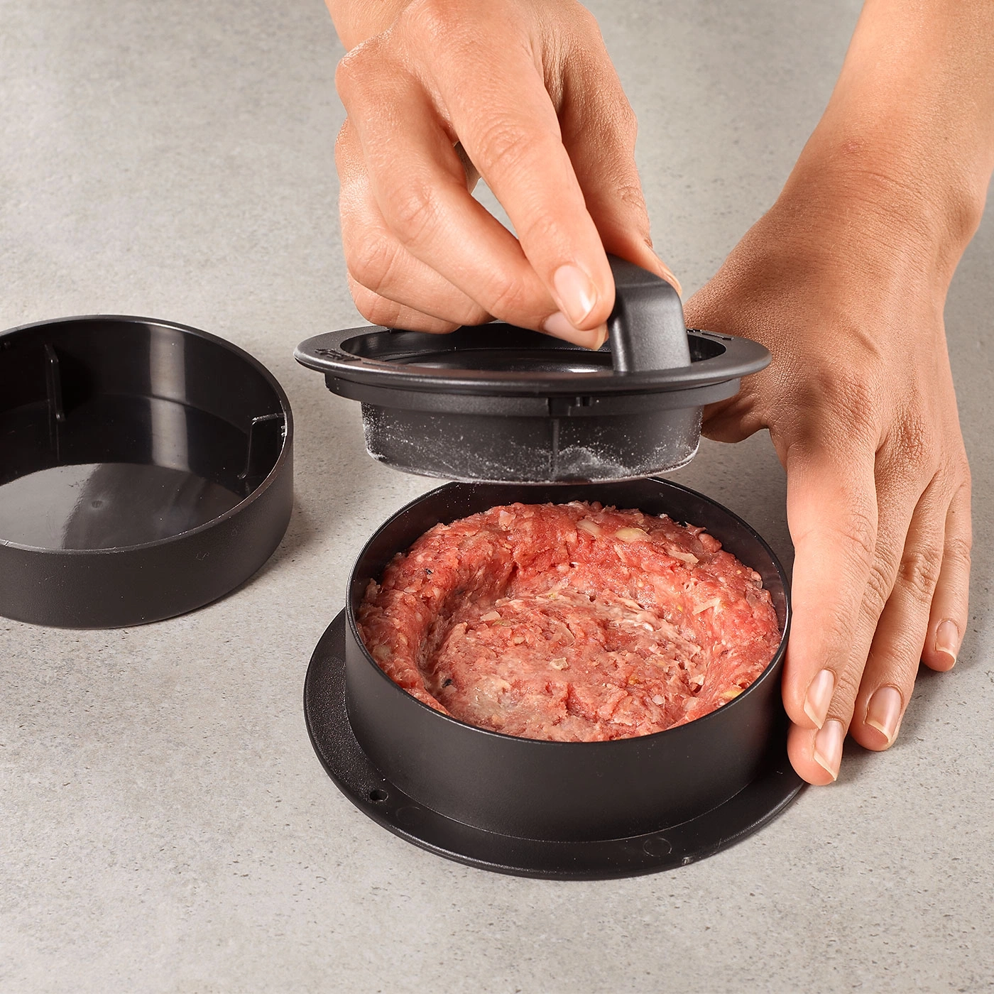 Personne façonnant un burger avec une presse à burger sur fond gris. Viande en forme.