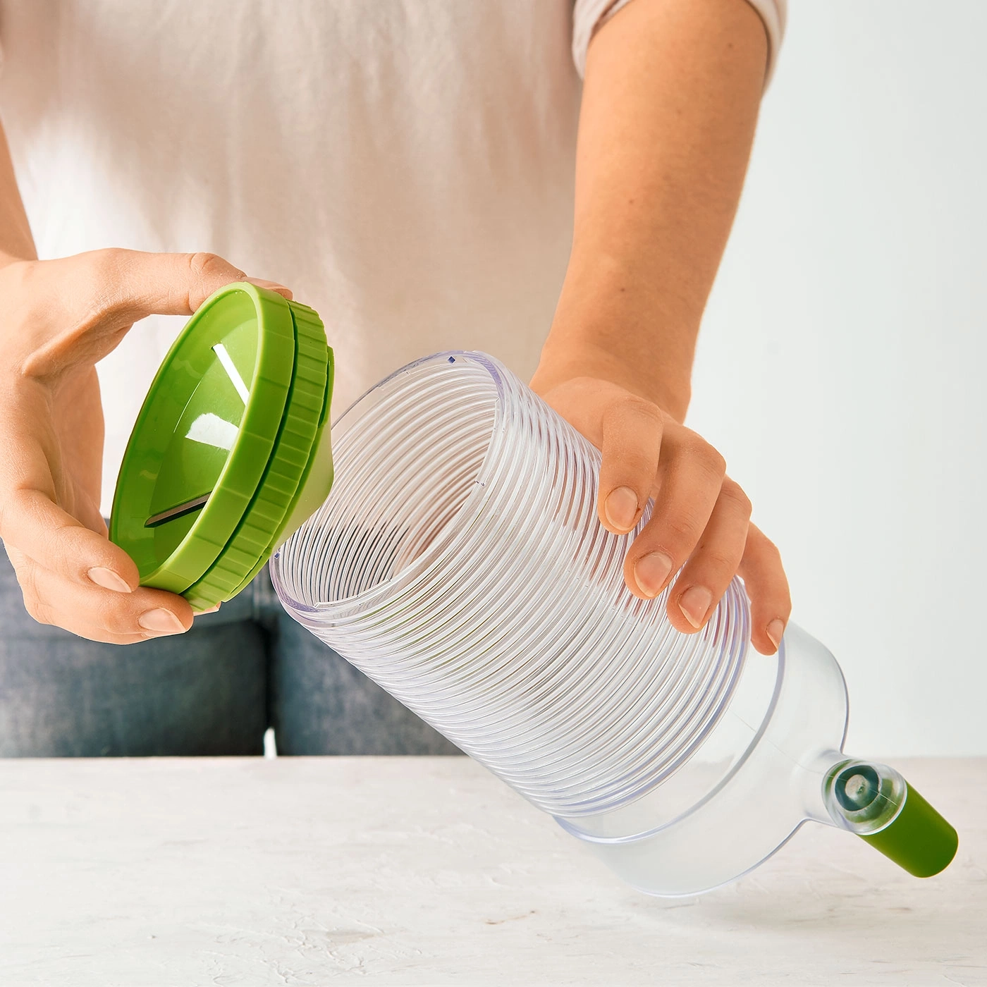 Personne tenant un ustensile de cuisine vert avec un récipient transparent et un couvercle.