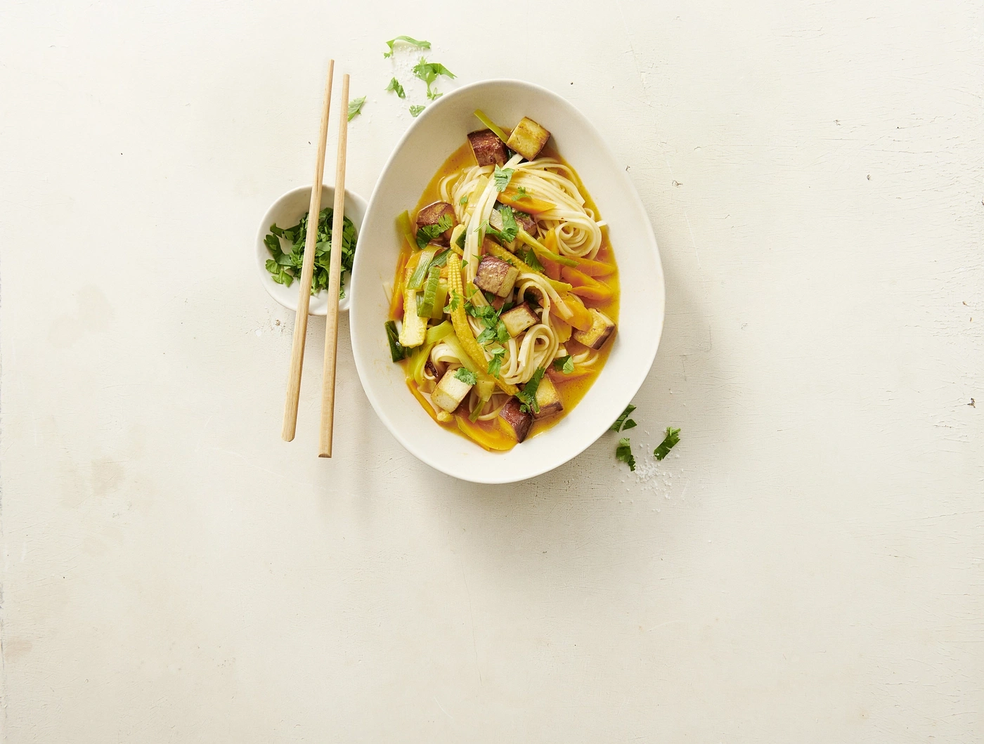 Eine Schüssel Nudelsuppe mit Tofu und Gemüse, daneben Stäbchen.