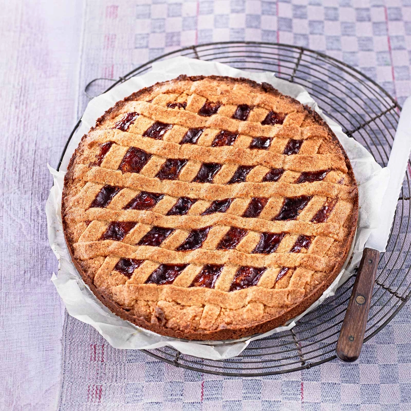 Kuchen mit Gittermuster auf einem Rost mit Messer auf kariertem Stoff