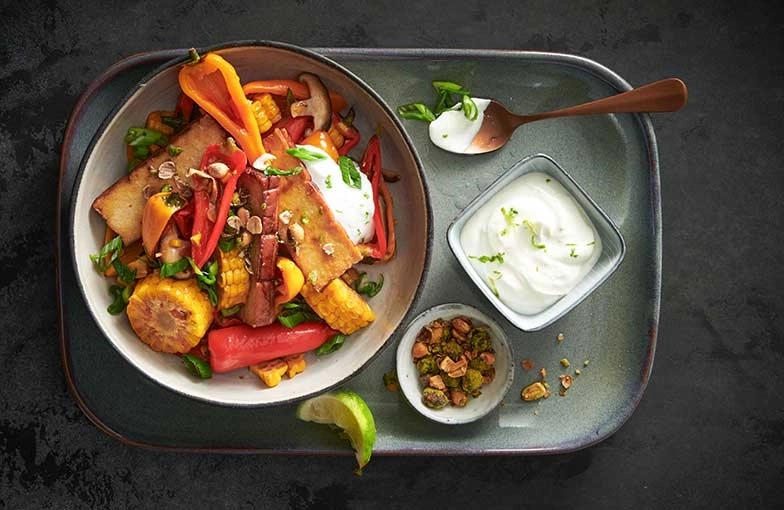 Plat de légumes avec tofu, maïs, sauce et citron vert sur un plateau