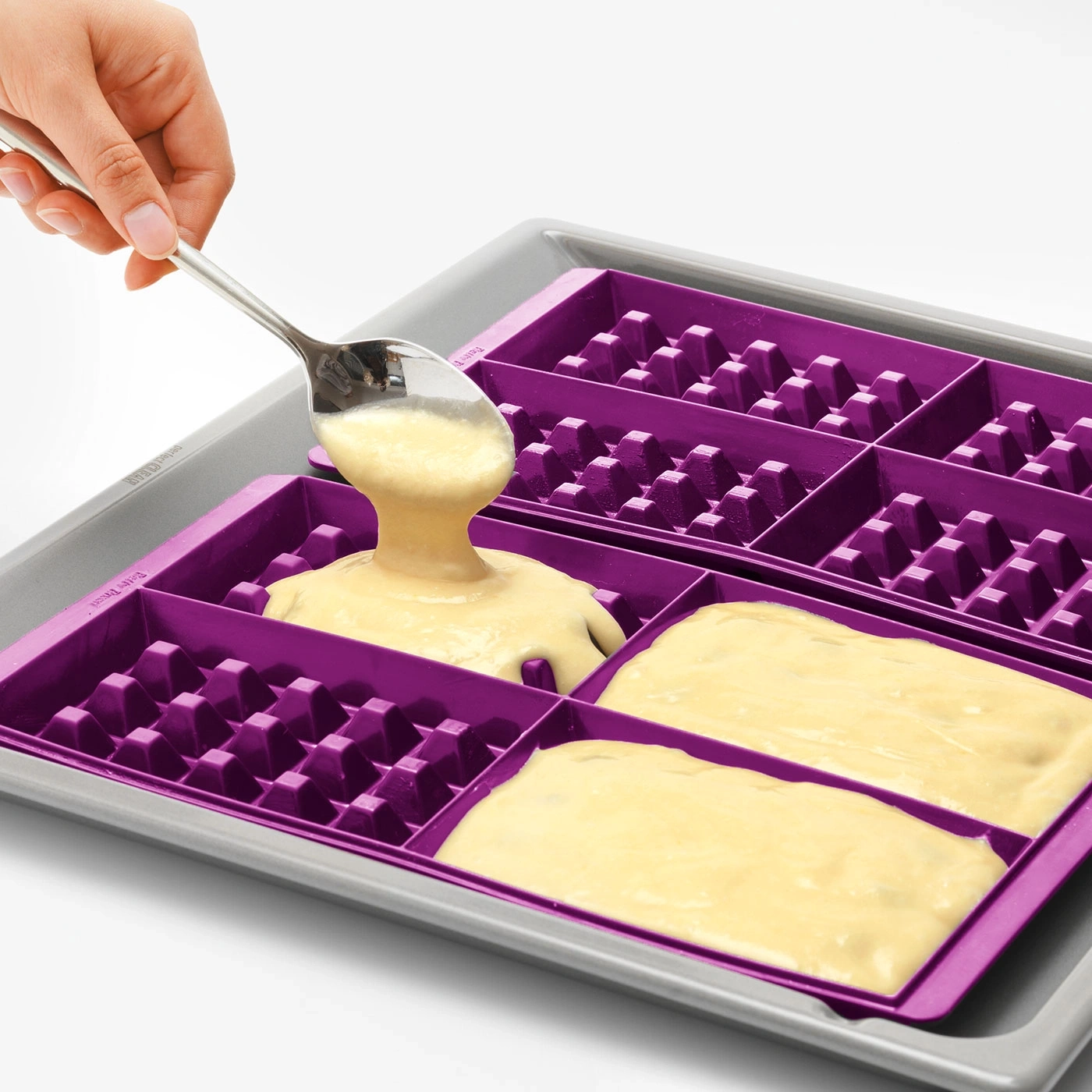 Eine Hand gießt Teig mit einem Löffel in eine Waffelform.