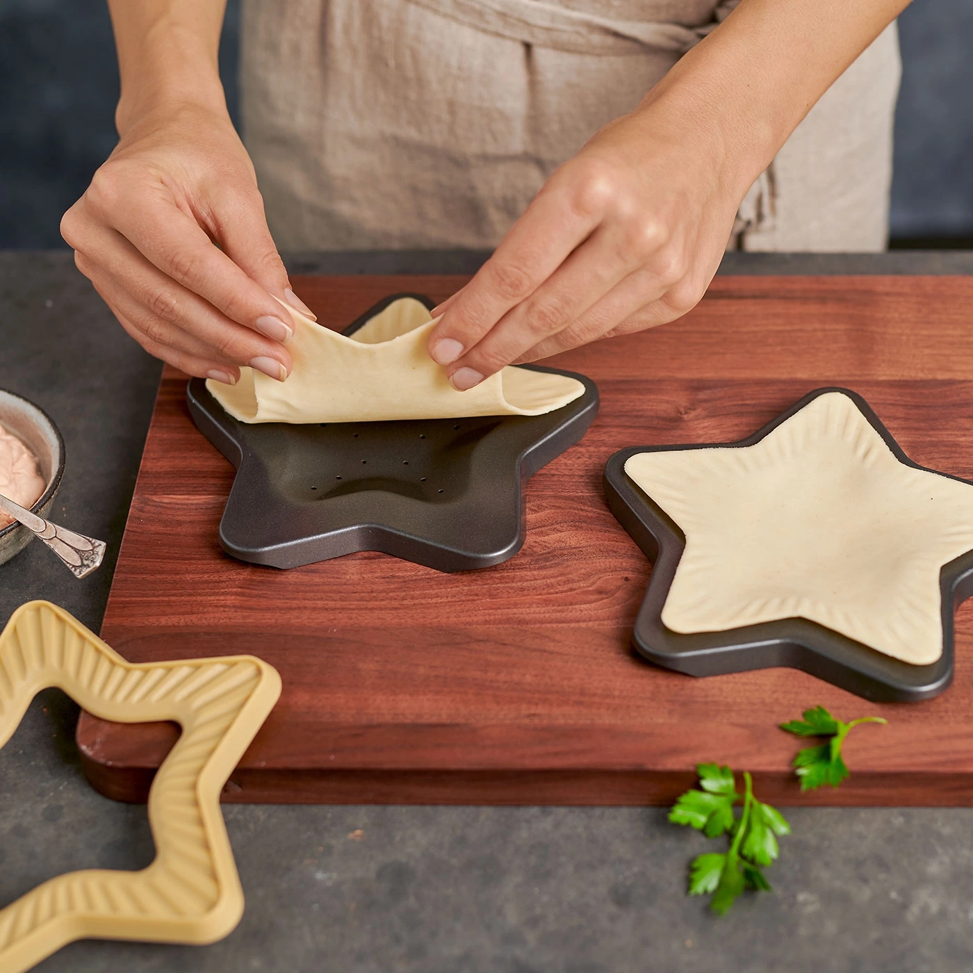Personne façonnant de la pâte en forme d'étoile. Sur planche de bois, avec des formes d'étoiles et du persil.