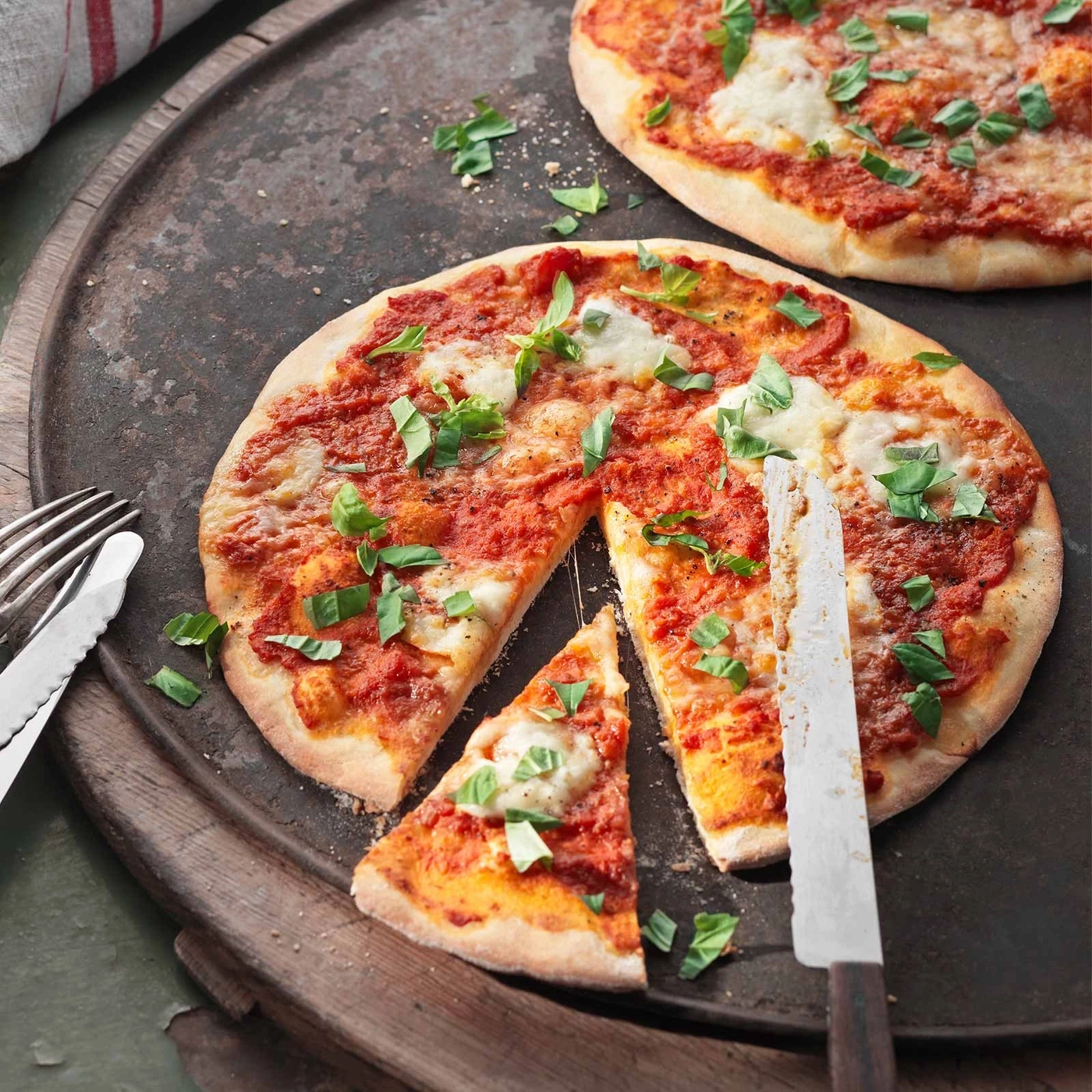 Pizza mit Tomatensauce, Käse und Basilikum auf einem Tablett mit Messer.
