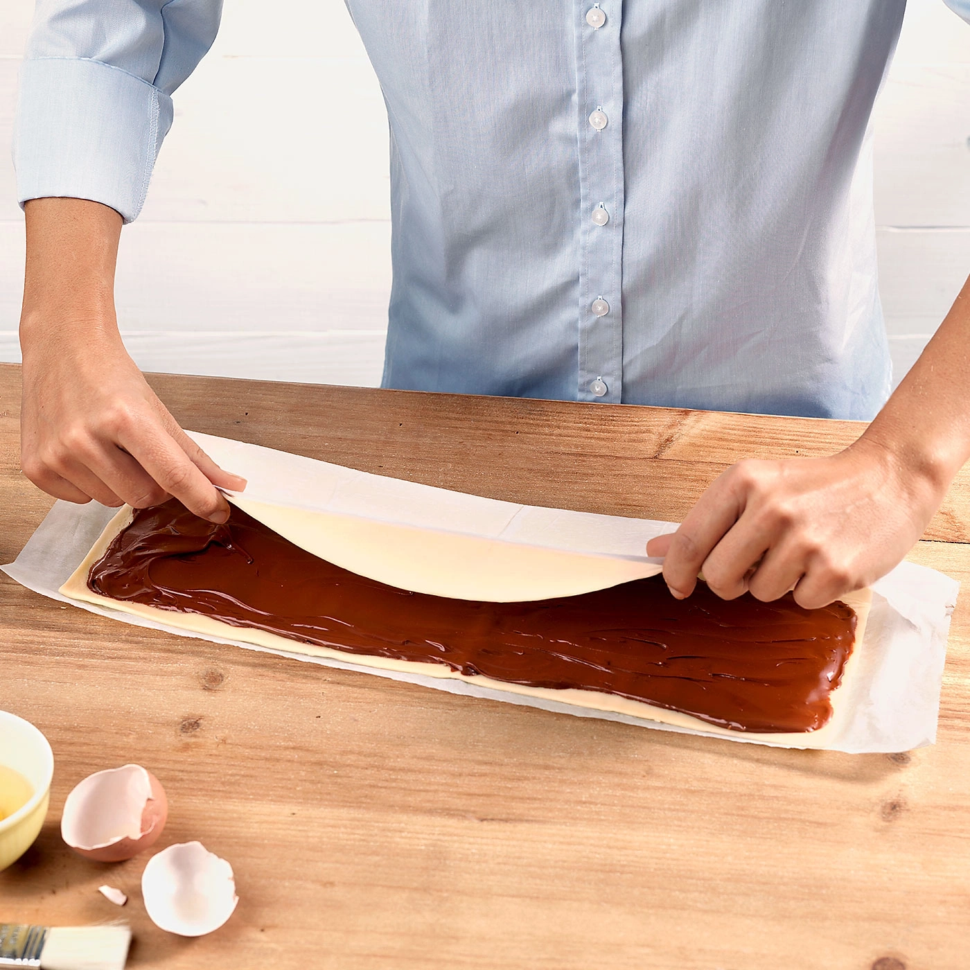 Person rollt Gebäck mit Schokoladenfüllung auf einem Holztisch ein.