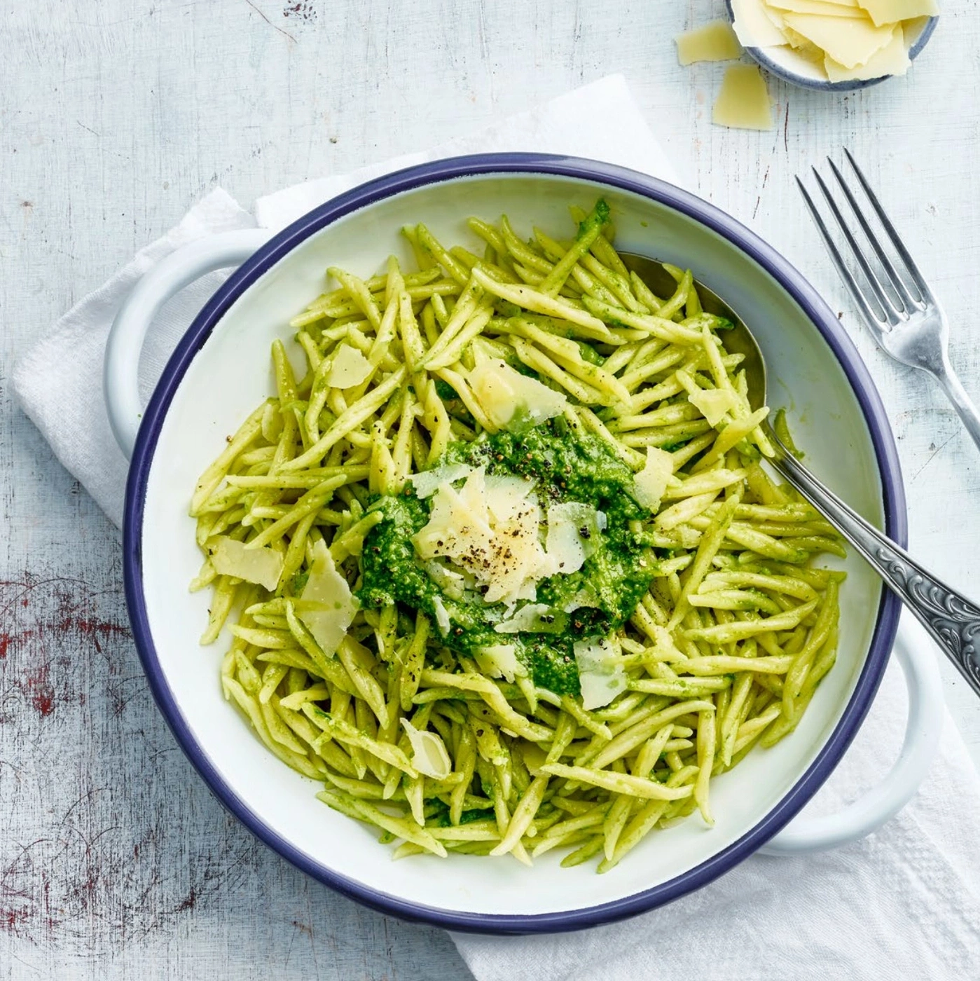 Pâtes vertes au pesto et parmesan dans un bol sur une table.