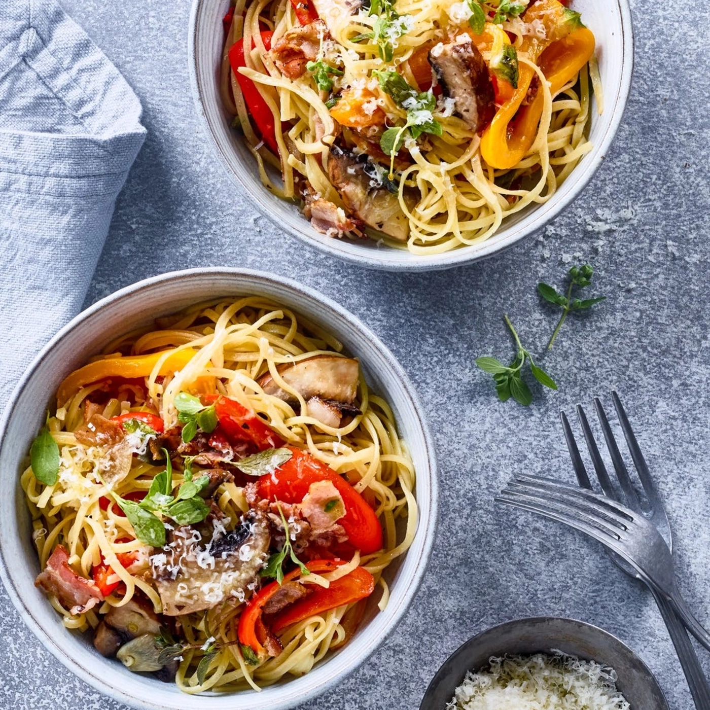 Zwei Schüsseln Pasta mit Gemüse und Käse, auf grauem Untergrund.