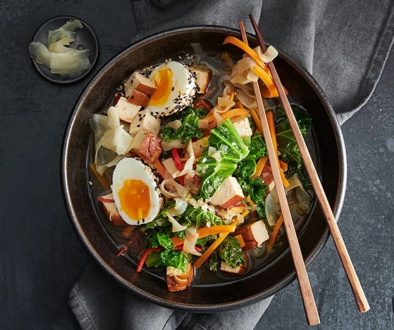 Schüssel Ramen mit Gemüse, Ei und Stäbchen auf grauem Hintergrund