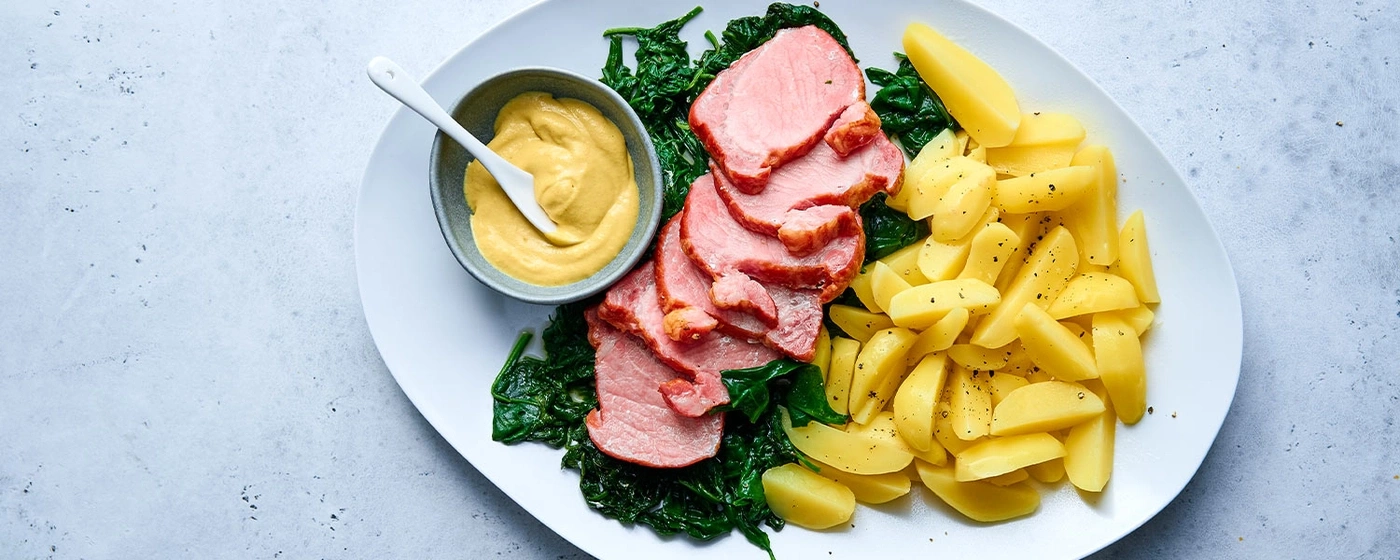 Gebratenes Fleisch mit Kartoffeln, Senf und Spinat auf einem Teller
