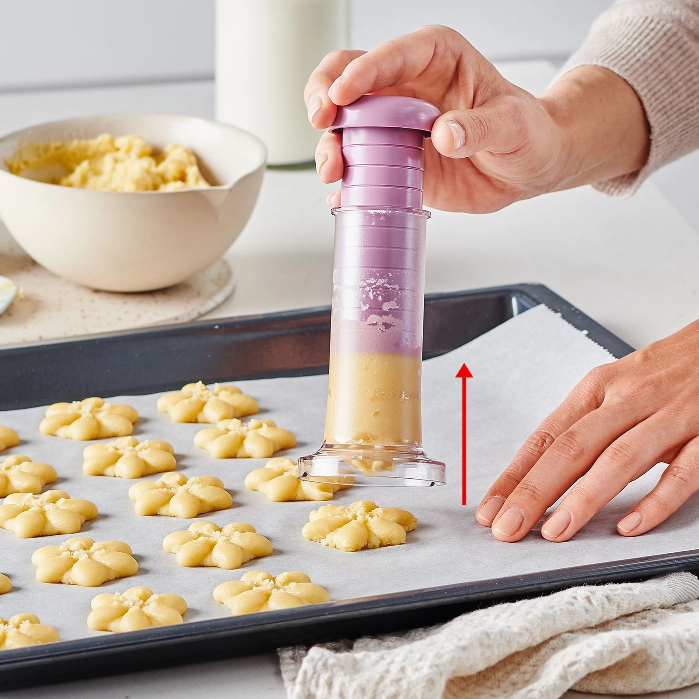 Une personne fait des biscuits avec un pistolet à biscuits sur une plaque à pâtisserie avec du papier sulfurisé.