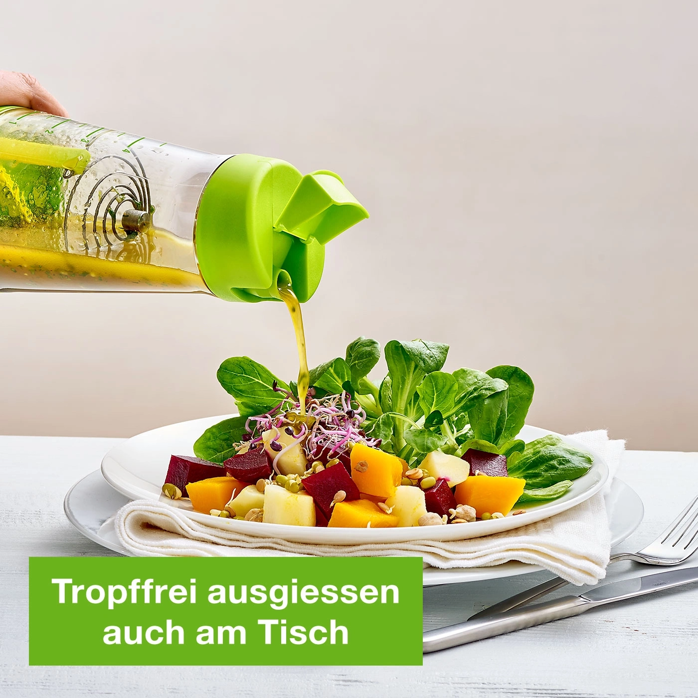 Salat wird mit Dressing aus einem grünen Behälter übergossen.