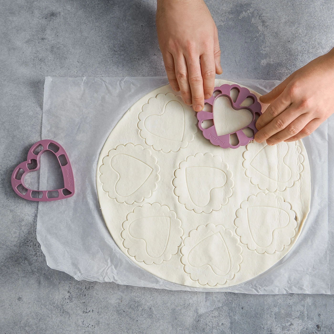 Hände schneiden Teig mit Herzform. Backen, Kochen, Küche, Werkzeug, Gebäck.