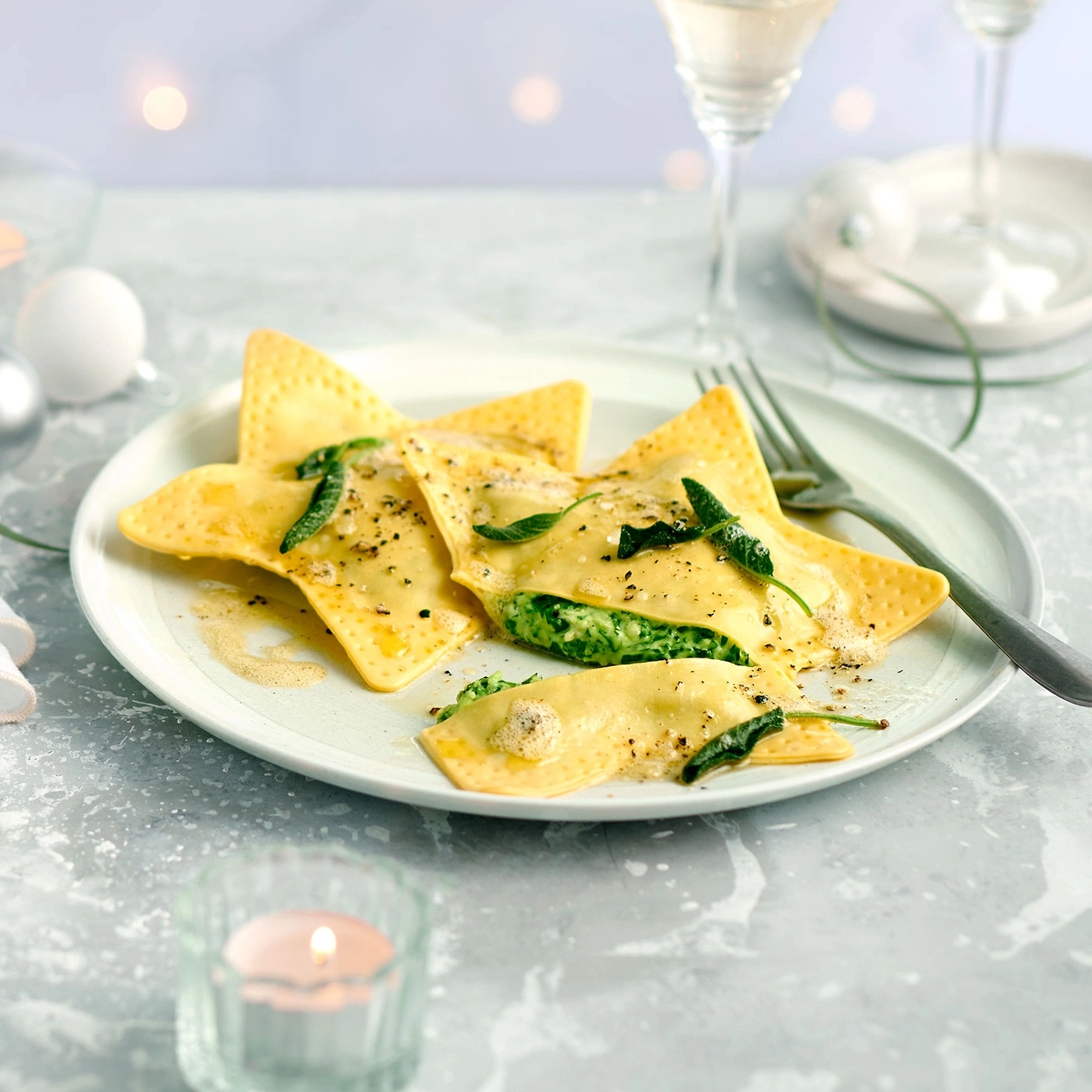 Raviolis en forme d'étoile sur une assiette, bougie et verres en arrière-plan.