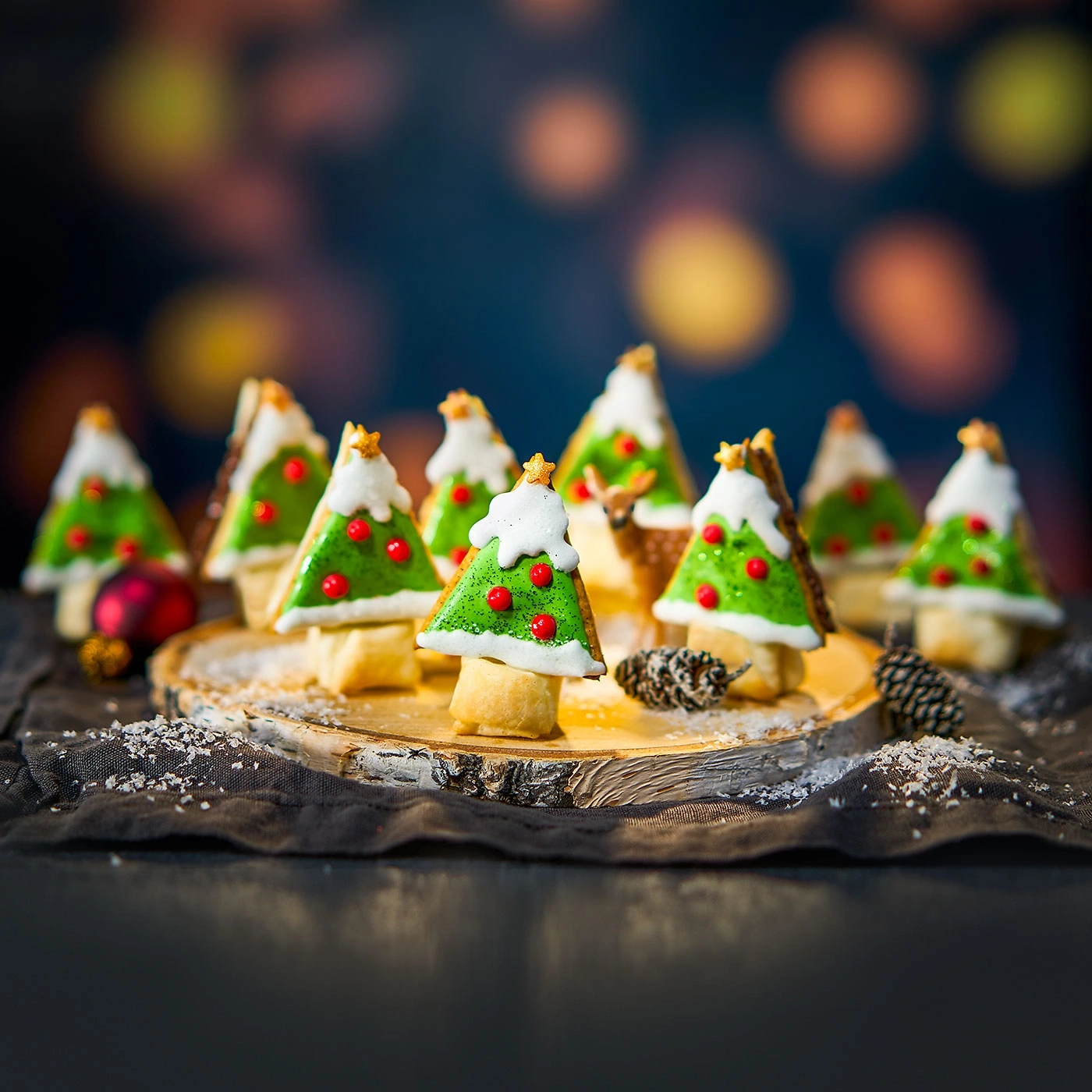 Weihnachtsbäume aus Gebäck auf einem Holzbrett mit Dekoration und Bokeh-Hintergrund.