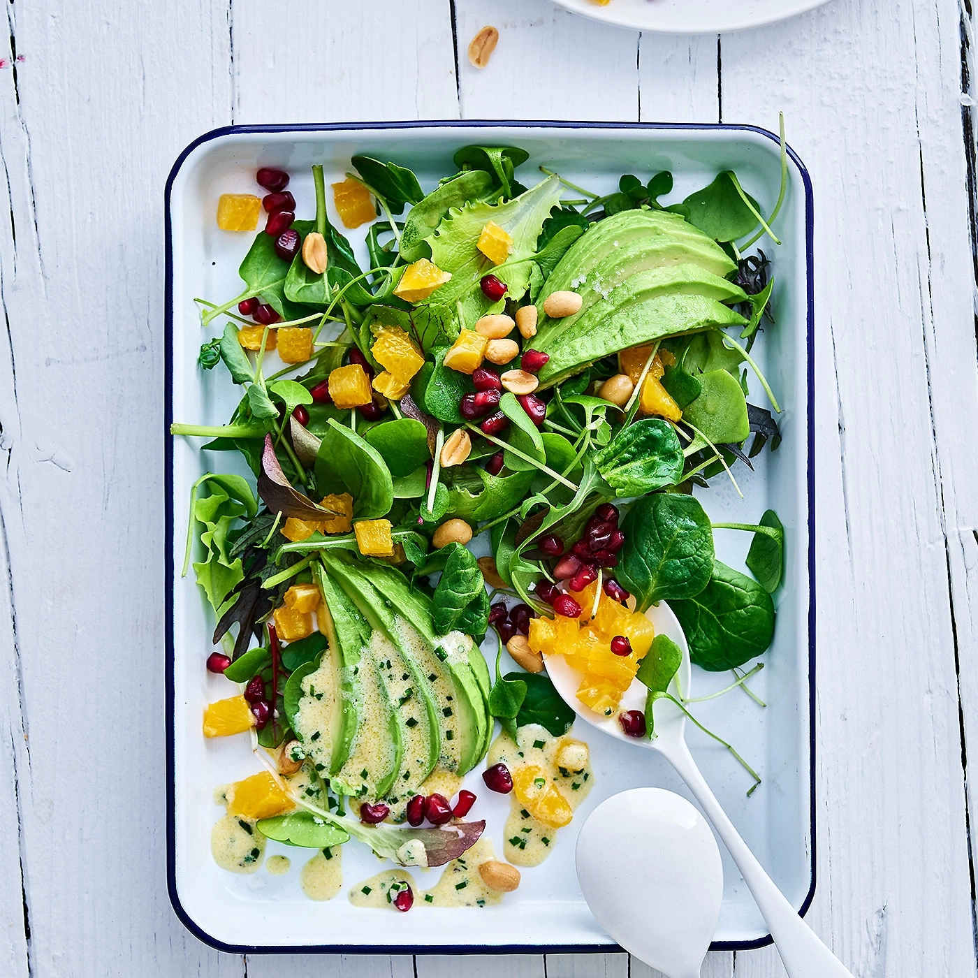 Salade d'avocat avec oranges, graines de grenade et cacahuètes sur plateau blanc