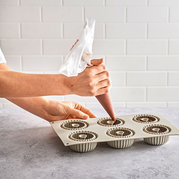Person füllt Kuchenformen mit Schokoladencreme. Backen, Küche, Handarbeit.
