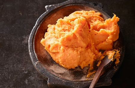 Nahaufnahme von Süßkartoffelpüree in einer Schüssel mit einem Löffel.