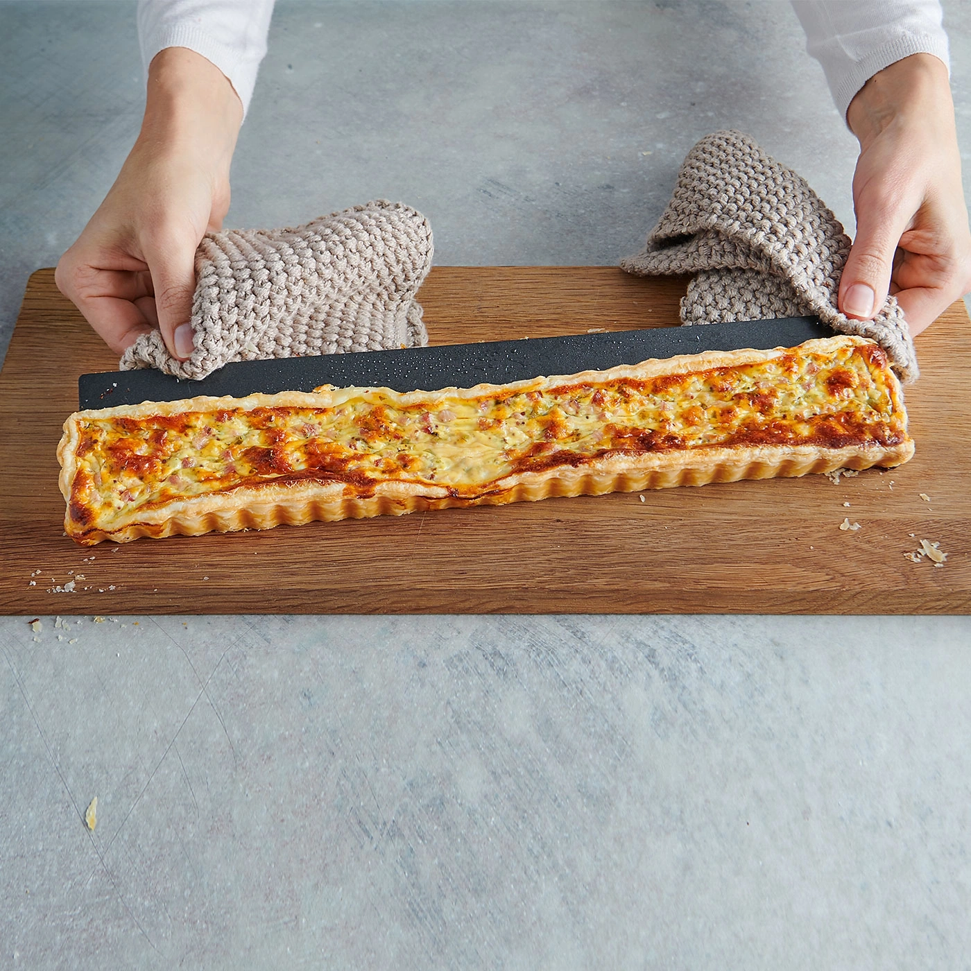 Person hält Quiche auf Holzbrett mit Topflappen, Nahaufnahme