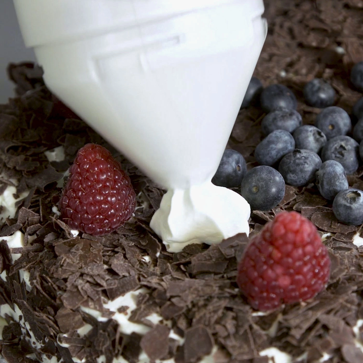 Schwarzwälder Kirschtorte mit Himbeeren, Blaubeeren und Sahne, die gerade aufgetragen wird.