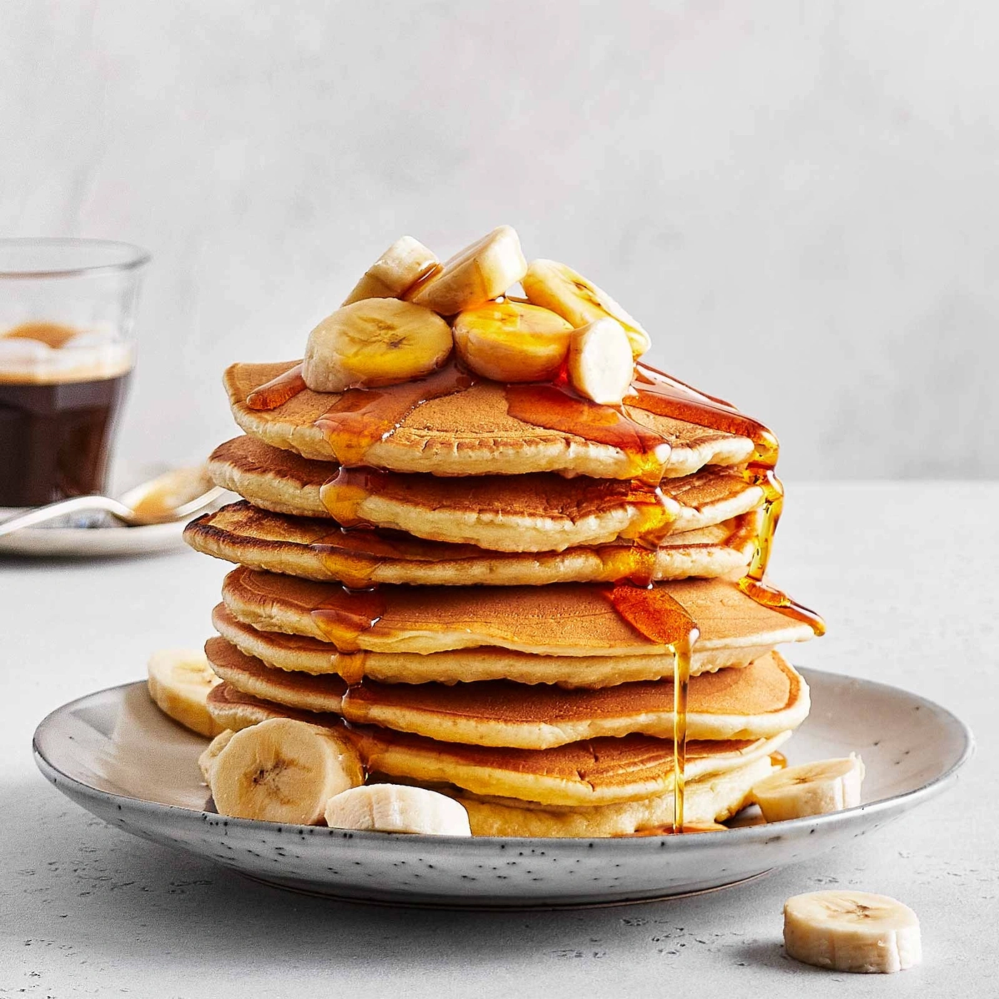 Ein Stapel Pfannkuchen mit Bananen und Sirup auf einem Teller.