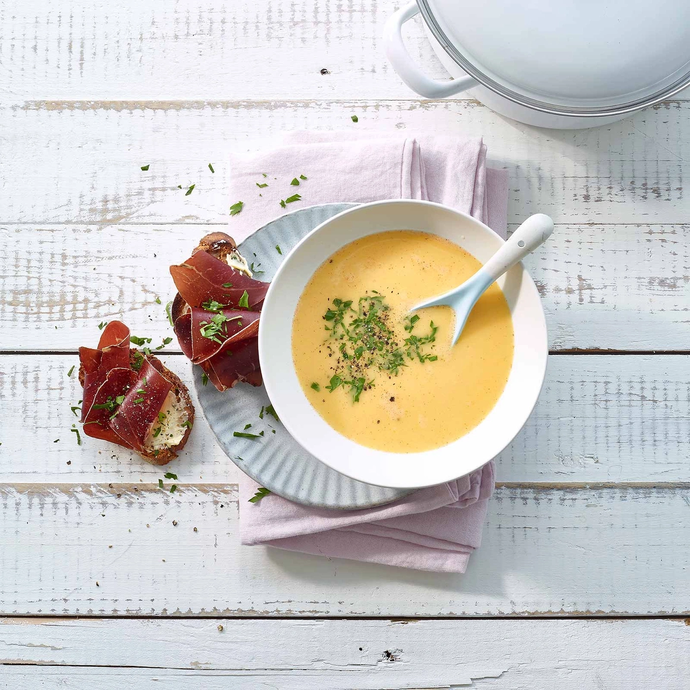 Suppe mit Brot und Schinken auf einem Holztisch