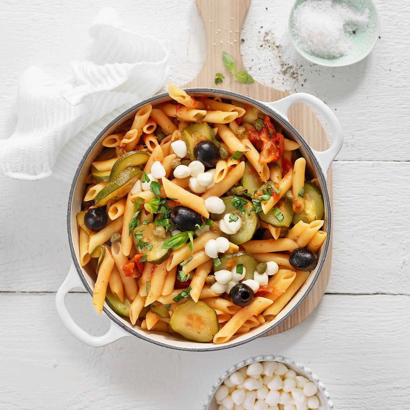Pasta mit Gemüse, Oliven und Mozzarella in einer Pfanne auf Holzbrett