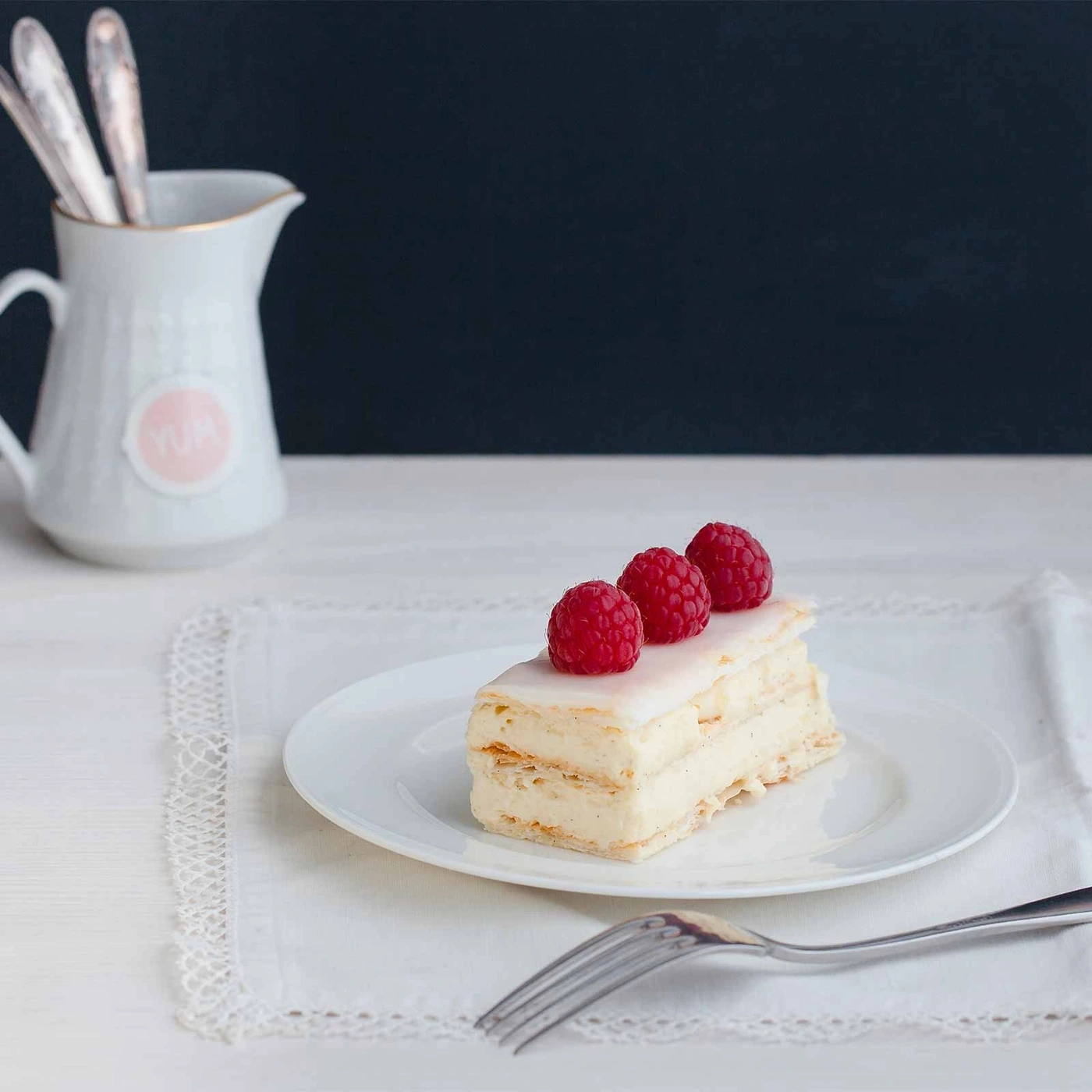 Kuchen mit Himbeeren auf einem Teller, daneben eine Kanne und eine Gabel.