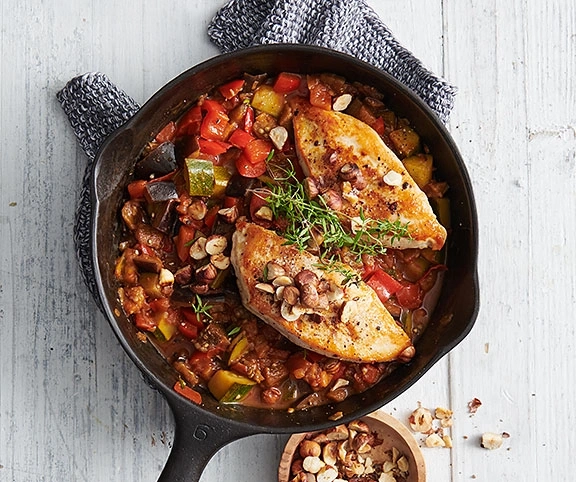 Hähnchen-Gemüse-Pfanne mit Haselnüssen in einer Pfanne auf Holz