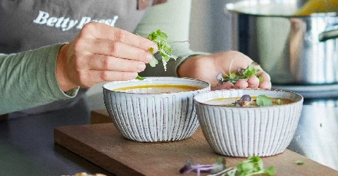Zwei Schalen Suppe, die mit Kräutern garniert wird, auf einem Holzbrett.