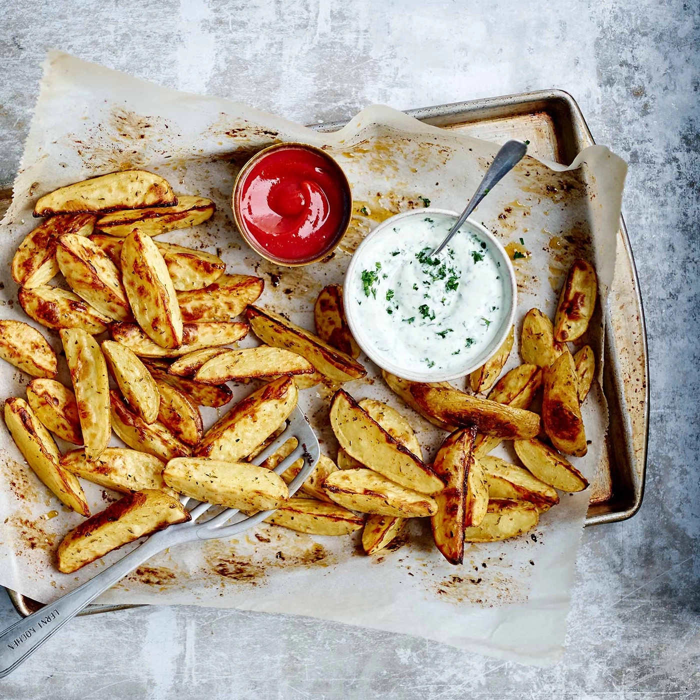 Knusprige Kartoffelspalten mit Soßen auf einem Backblech