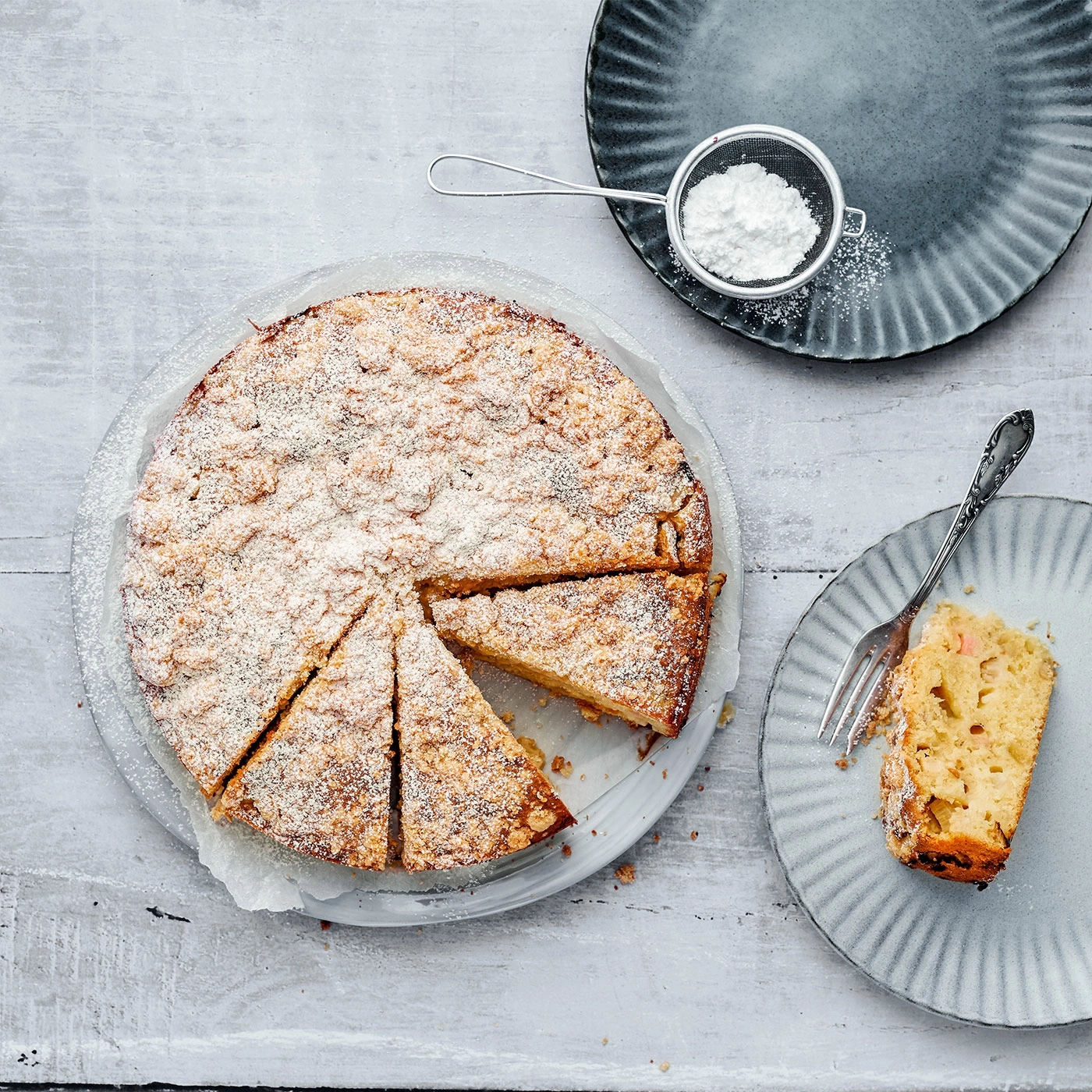 Kuchen mit Puderzucker, auf einem Teller serviert, mit Gabel und Sieb.