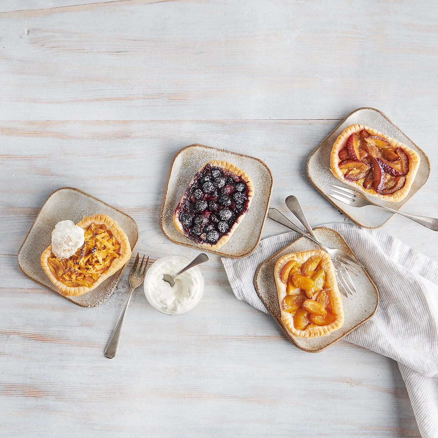 Tartes aux fruits sur assiettes, avec fourchettes et crème, sur fond bois