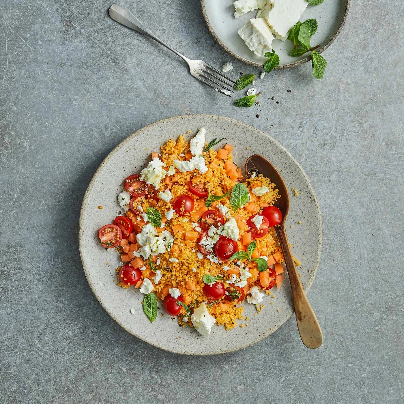 Couscous-Salat mit Tomaten, Feta und Minze auf einem Teller mit Löffel