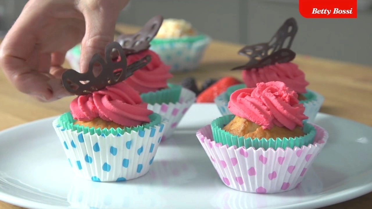 Cupcakes avec crème rose et décoration papillon sur une assiette.