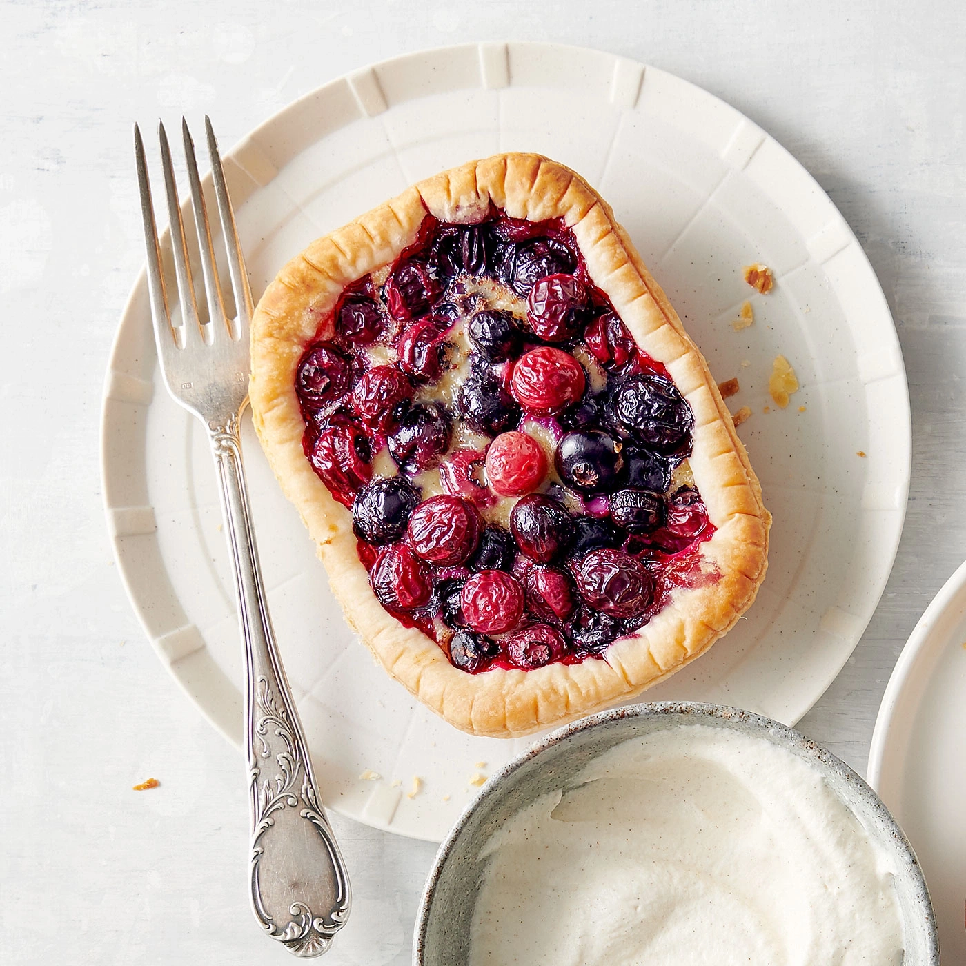 Tarte aux baies sur une assiette avec fourchette et crème, gros plan