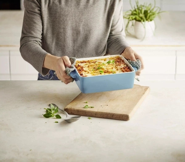 Eine Person hält eine Lasagne in einem blauen Auflaufform in der Hand