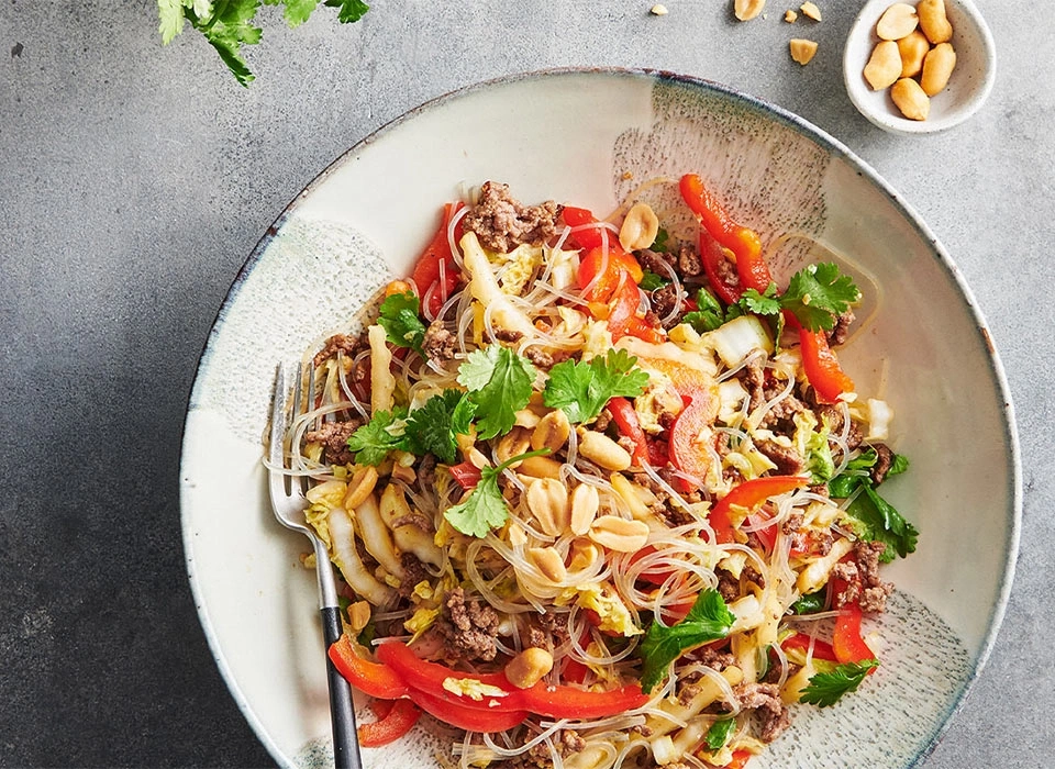 Asiatisches Gericht mit Nudeln, Gemüse, Fleisch und Erdnüssen in einer Schüssel.