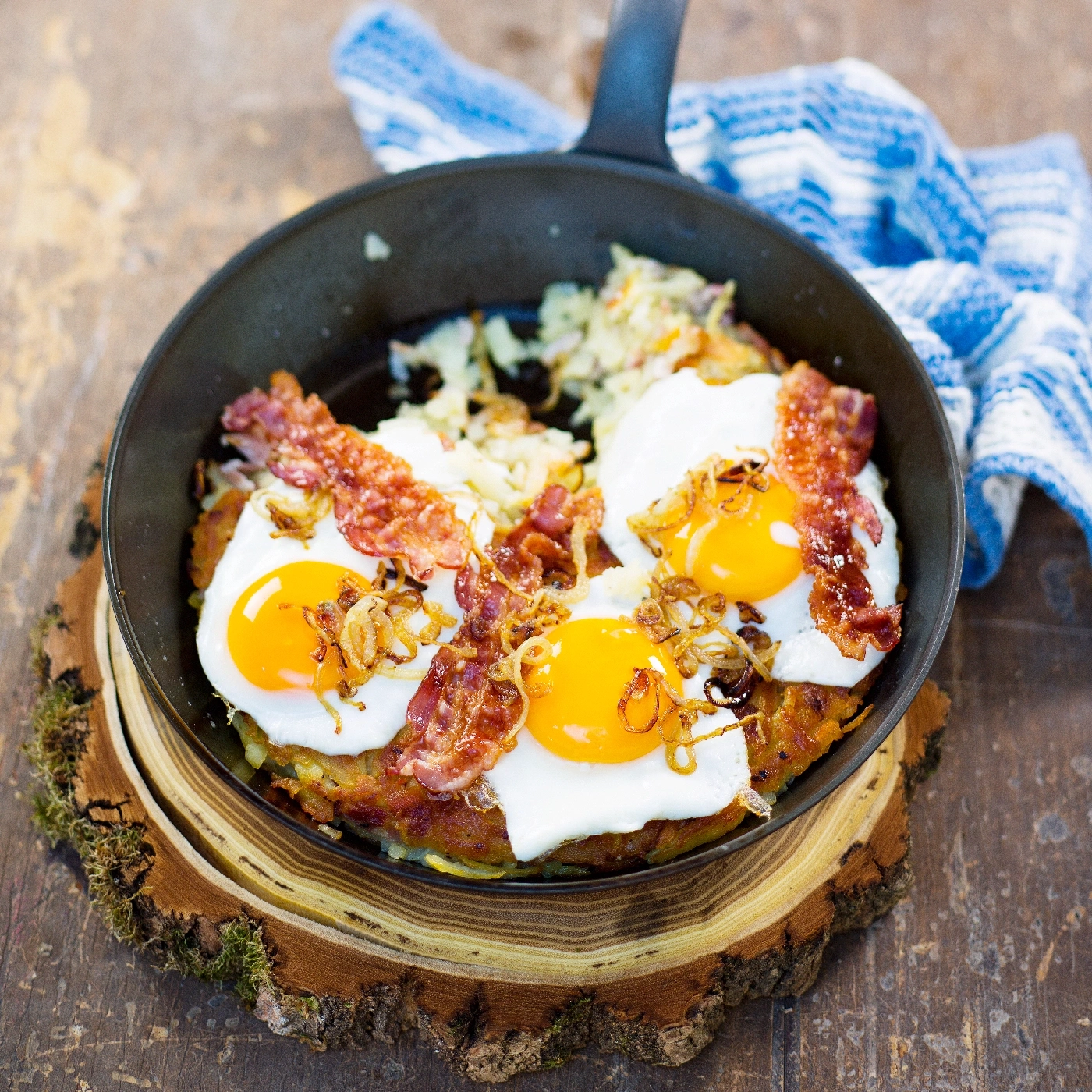 Gebratene Eier mit Speck und Zwiebeln in einer Pfanne auf Holzbrett
