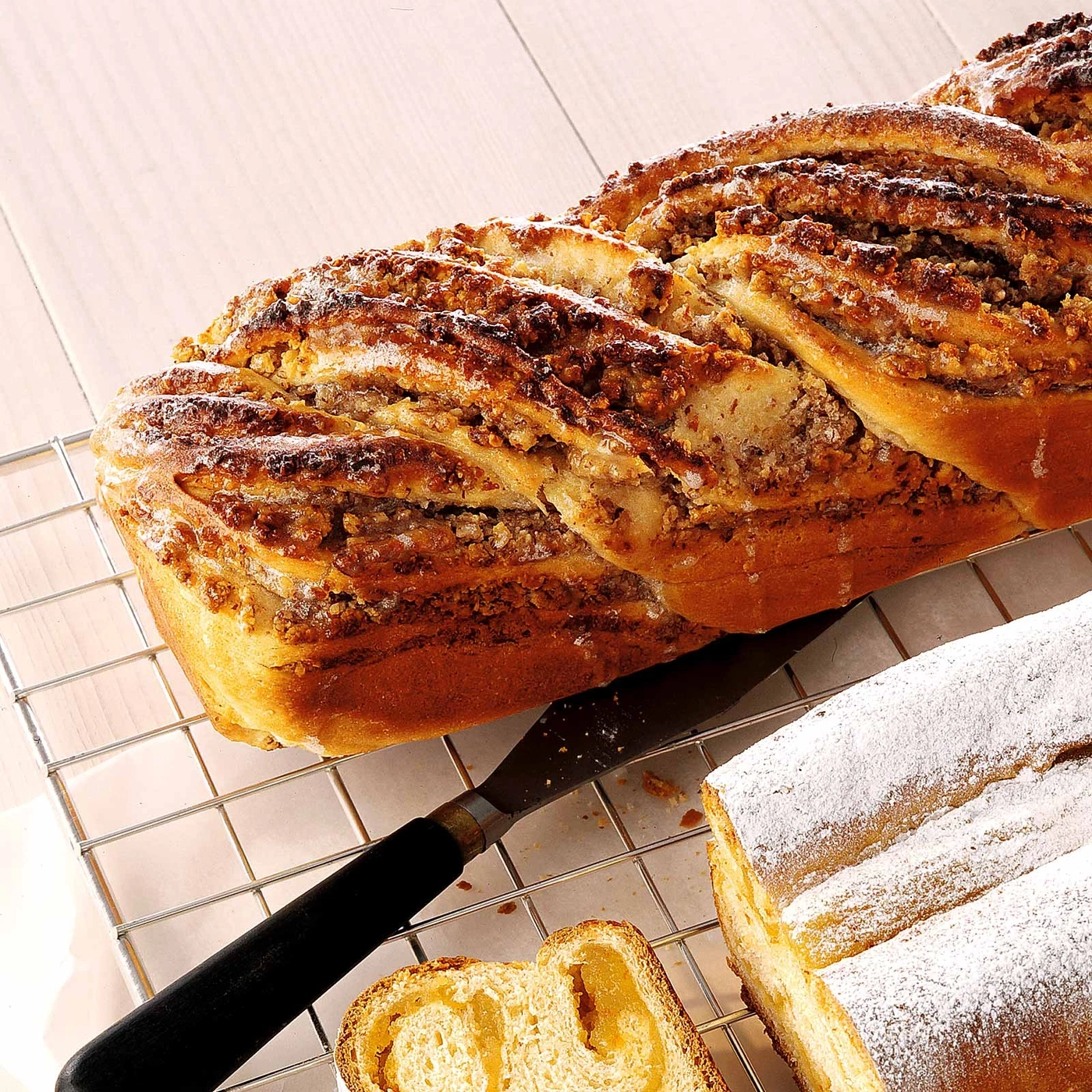 Geflochtener Kuchen mit Nüssen und Puderzucker, auf einem Gitter, mit Messer und Scheibe