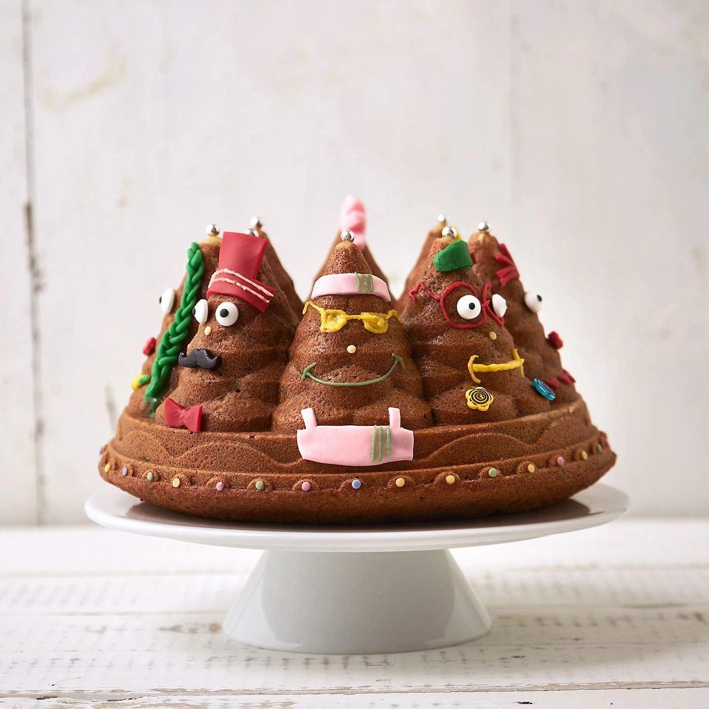 Gâteau avec des visages, sur un présentoir à gâteau blanc, décoré de décorations en sucre.