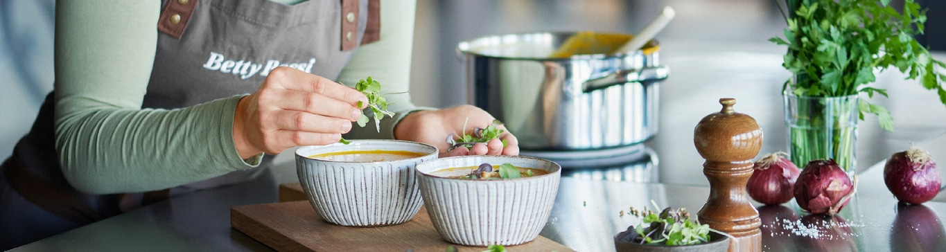 Person garniert Suppe mit Kräutern. Küchenszene mit Zwiebeln und Gewürzen.