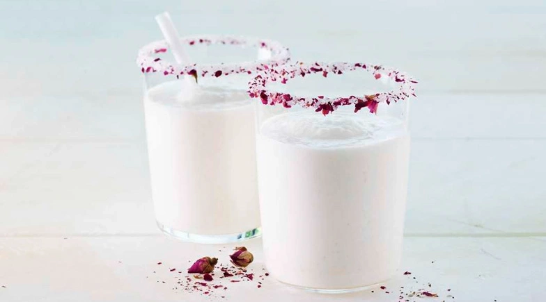 Zwei Gläser mit rosa Blütenblättern am Rand, Milchgetränk, weißer Hintergrund.