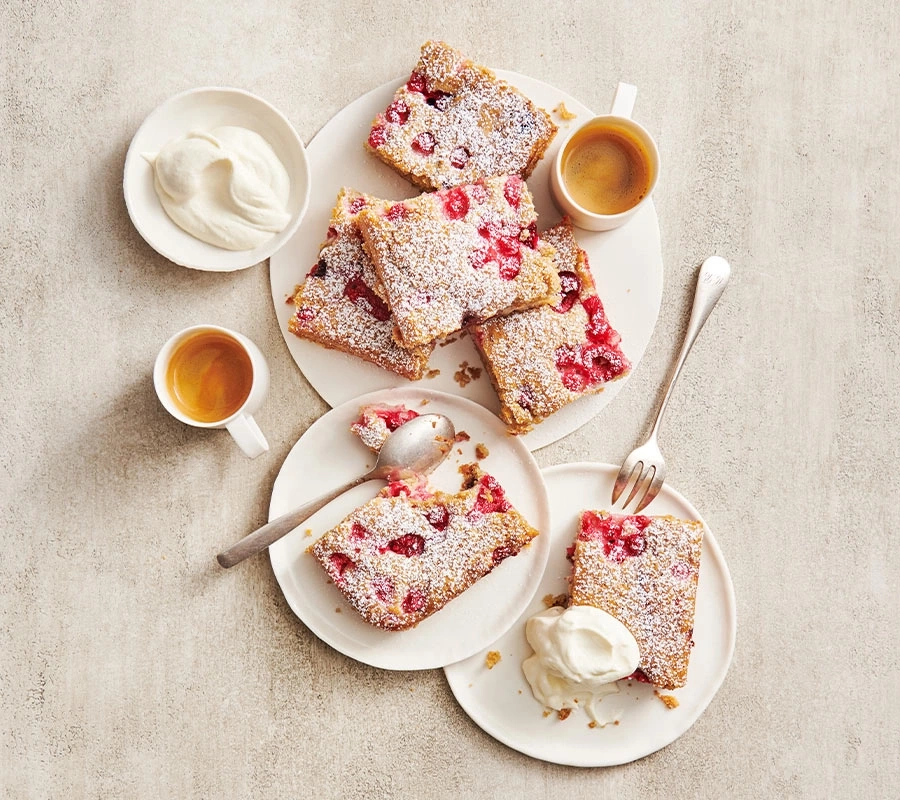 Kuchen mit Beeren, Puderzucker, Sahne und Kaffee auf Tellern serviert.